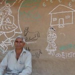 Kalubhai Wala with a village painting behind him.